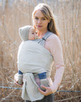 Frau trägt Baby in den Loops mit dem Übertuch "sand", Schilfgras im Hintergrund.