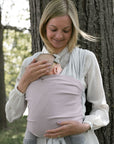 Frau trägt Baby in den Loops mit dem Übertuch "blossom", stehend vor einem Baum.