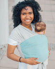 Frau trägt Baby in den Loops mit dem Übertuch "ocean", heller Hintergrund.