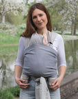 Frau trägt Baby in den Loops mit dem Übertuch "night blue", Fluss und Bäume im Hintergrund.