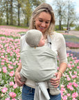 Frau trägt Baby in den Loops mit dem Übertuch "jade", Blumenwiese im Hintergrund.