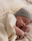 schlafendes Baby mit Strickmütze, eingewickelt in naturfarbene Babydecke