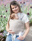 Frau trägt Baby in unseren Loops mit einem "hazel" Übertuch und sitzt vor einem Tulpenfeld.
