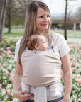 Frau trägt Baby in Loops mit Übertuch in "hazel", im Hintergrund eine Blumenwiese.