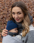Frau mit Baby in der Trage, beide tragen einen Fleece-Loopschal in "anthrazit", steht im Herbstwald