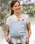 Frau trägt Baby in den Loops mit dem Übertuch "sky blue", Baumzweige im Hintergrund.