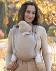 Frau trägt Baby in Loops in "toffee" ohne Übertuch, herbstlicher Hintergrund.