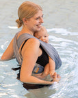 Frau trägt Baby in AQUA Loops in "ocean", sie steht seitlich bis zur Hüfte im Wasser.