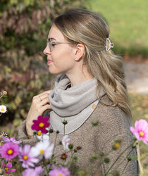 Frau trägt einen grauen Fleece-Schal aus der Zubehör-Kollektion, umgeben von bunten Blumen.