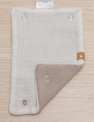 Gurtschoner in beige Musselin und Innenseite in ecru Fleece, geöffnet und eine Ecke gefaltet, liegt auf Holzhintergrund