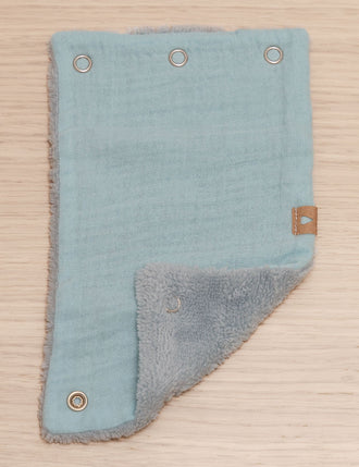Gurtschoner in blau Musselin und Innenseite blau Fleece, geöffnet und eine Ecke gefaltet, liegt auf Holzhintergrund