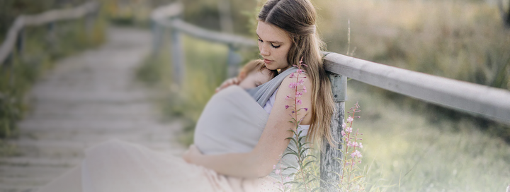 Mutter sitzt draußen auf einem Holzsteg und trägt ihr Baby in unseren Loops TO GO