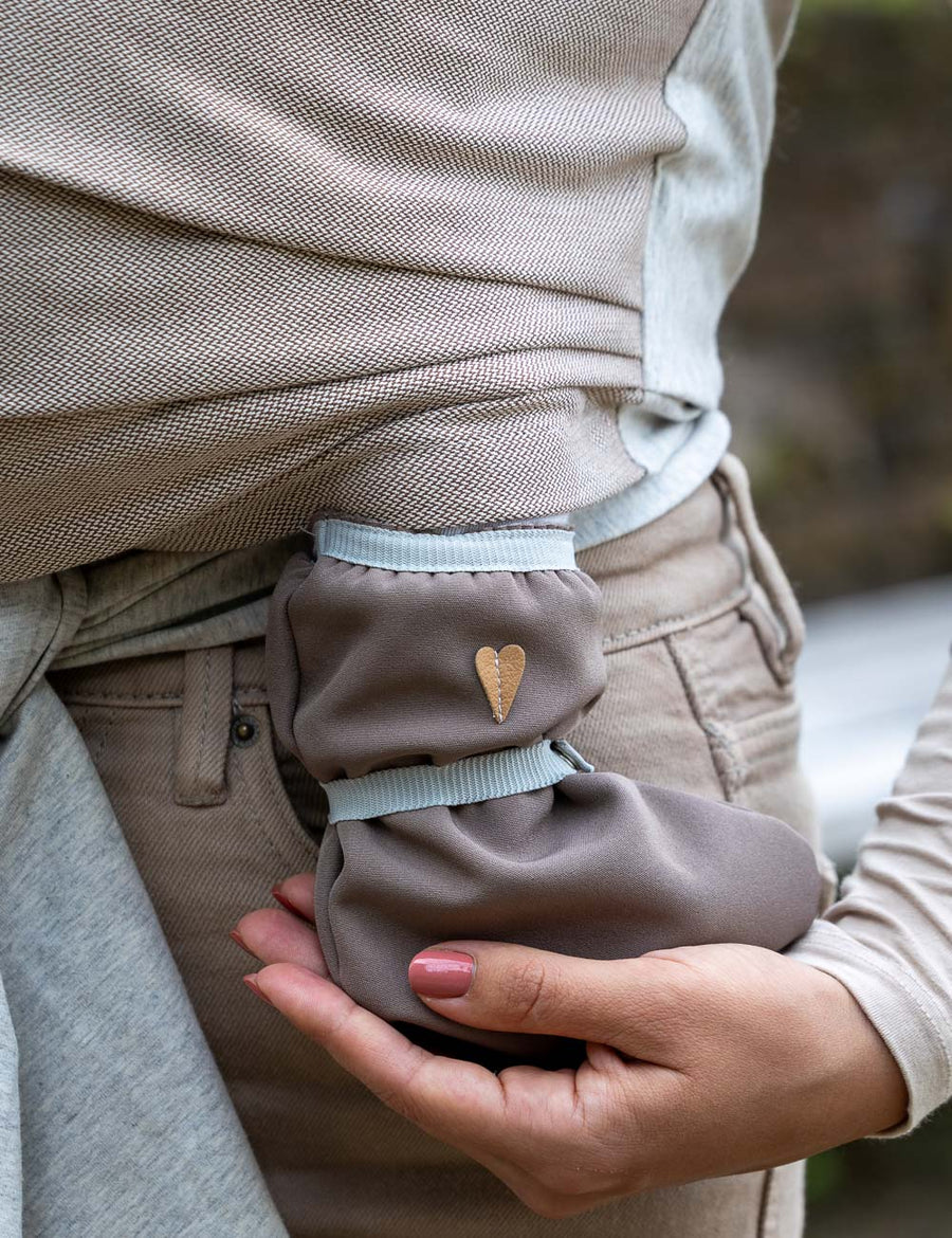 Nahaufnahme - Babyfüße in braunen Softshellschuhen, Baby wird dabei in Loops getragen