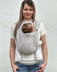 Frau trägt Baby in den Loops ohne Übertuch, die Nackenrolle ist in Benutzung und auch das Knopfgummi, dieses rafft einen Loop auf Kopfhöhe des Babys zusammen
