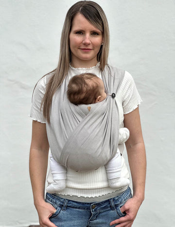 Frau trägt Baby in den Loops ohne Übertuch, die Nackenrolle ist in Benutzung und auch das Knopfgummi, dieses rafft einen Loop auf Kopfhöhe des Babys zusammen